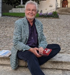 Ein Mann mit Bart und Brille sitzt auf einer Treppe und hat ein Smartphone in der Hand.