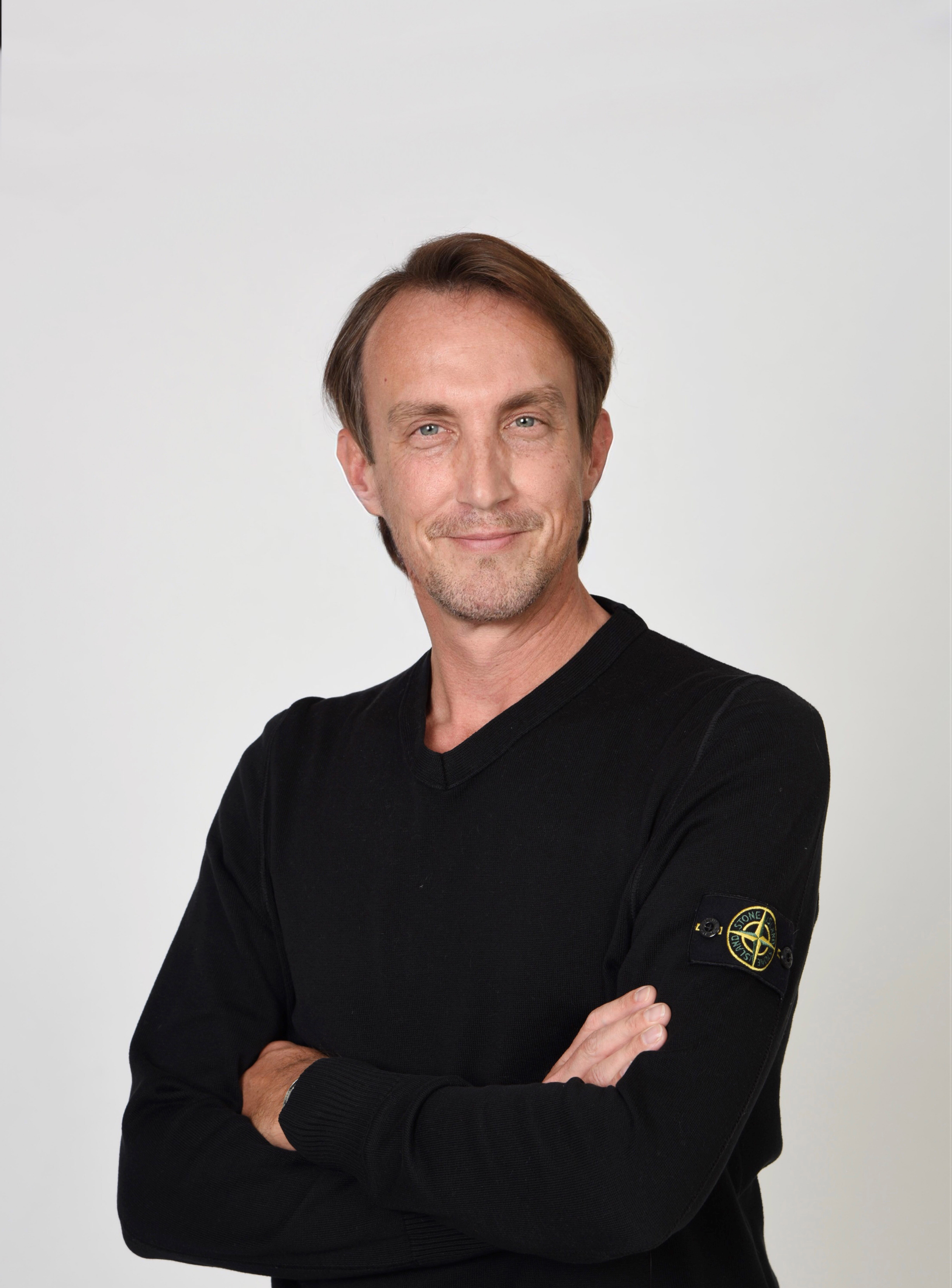 Portrait photo of a friendly smiling man in a black jumper with his arms folded.