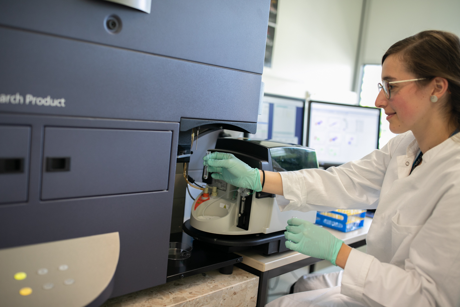 A woman in a white coat operates a flow cytometer.