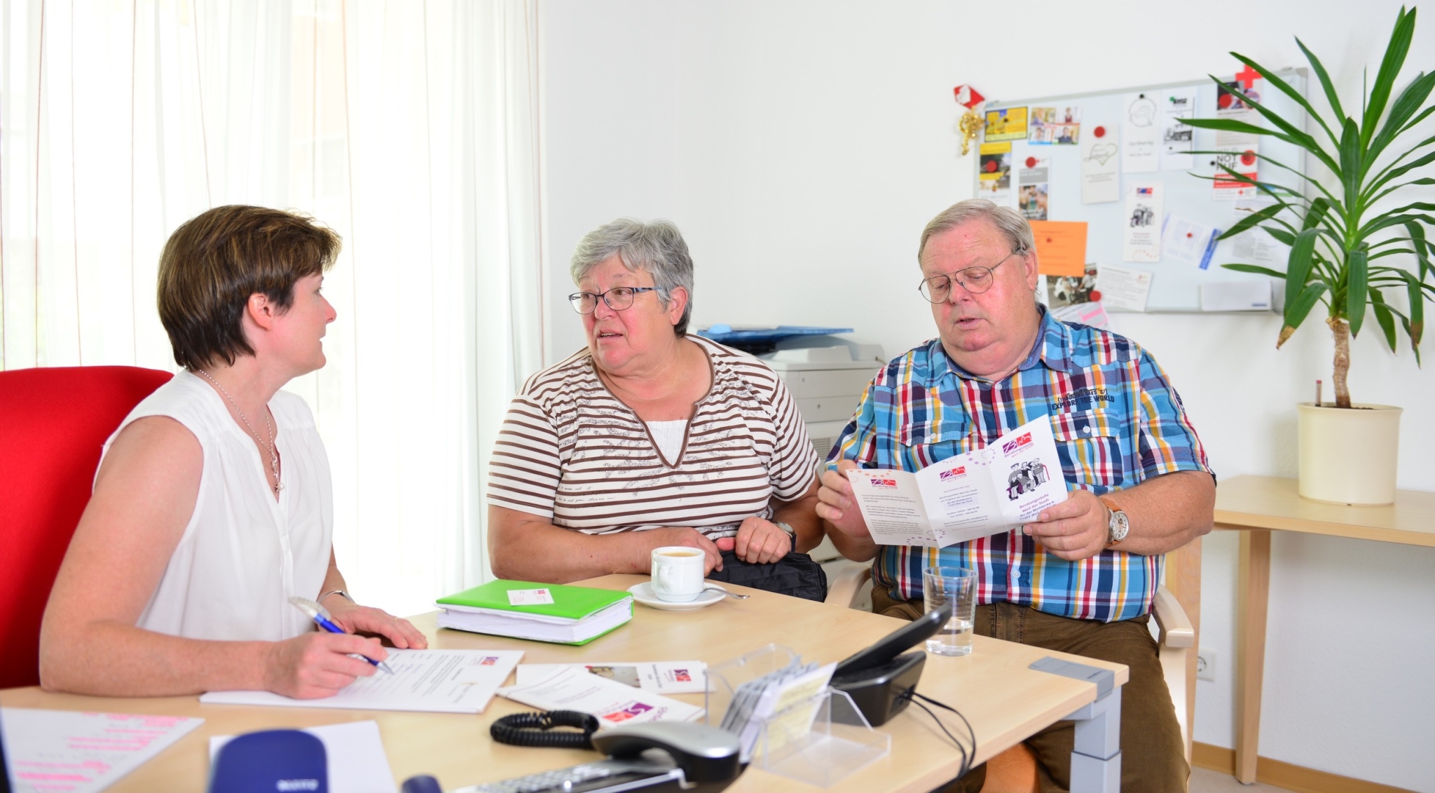 Die Beratungssituation zeigt ein Paar, dass mit einer Beraterin an einemTisch sitzt. Auf dem Tisch liegen diverse Dokumente und Flyer, die zurBeratung mit herangezogen werden.