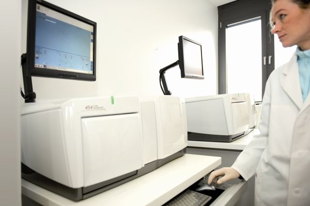 Laboratory assistant standing in front of a computer and looking onto a screen and analysing the data shown.