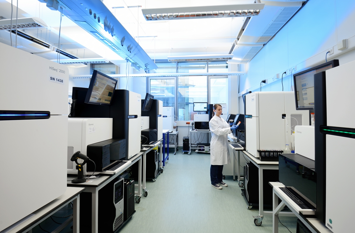 Woman wearing a white lab coat in a laboratory looking at a tube she is holding in her hand.