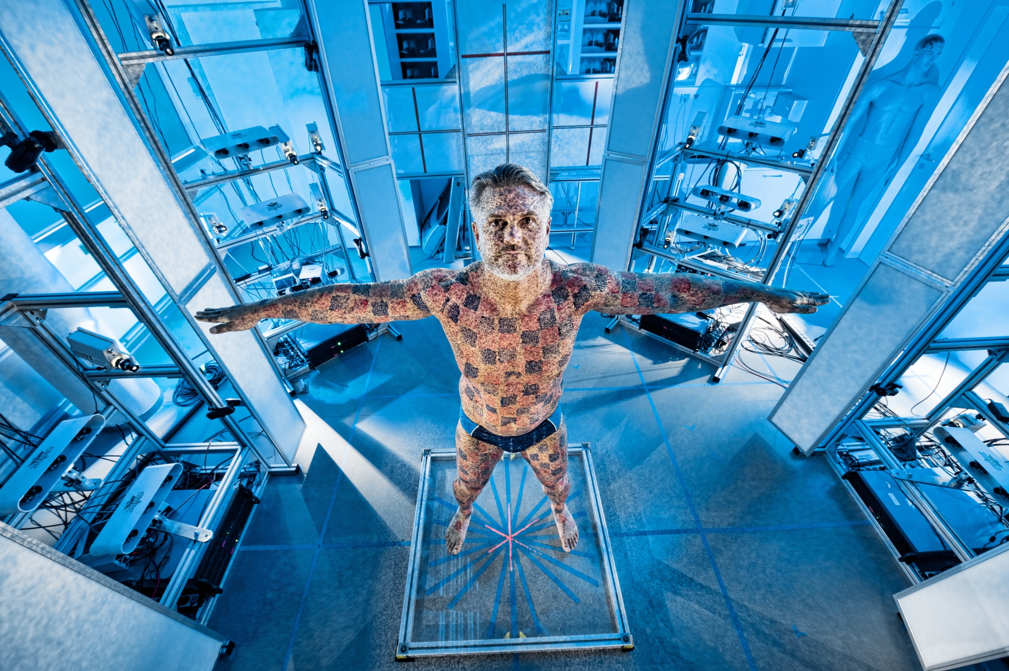 Man standing in a full-body scanner in a laboratory. The man's body is illuminated with blue squares.