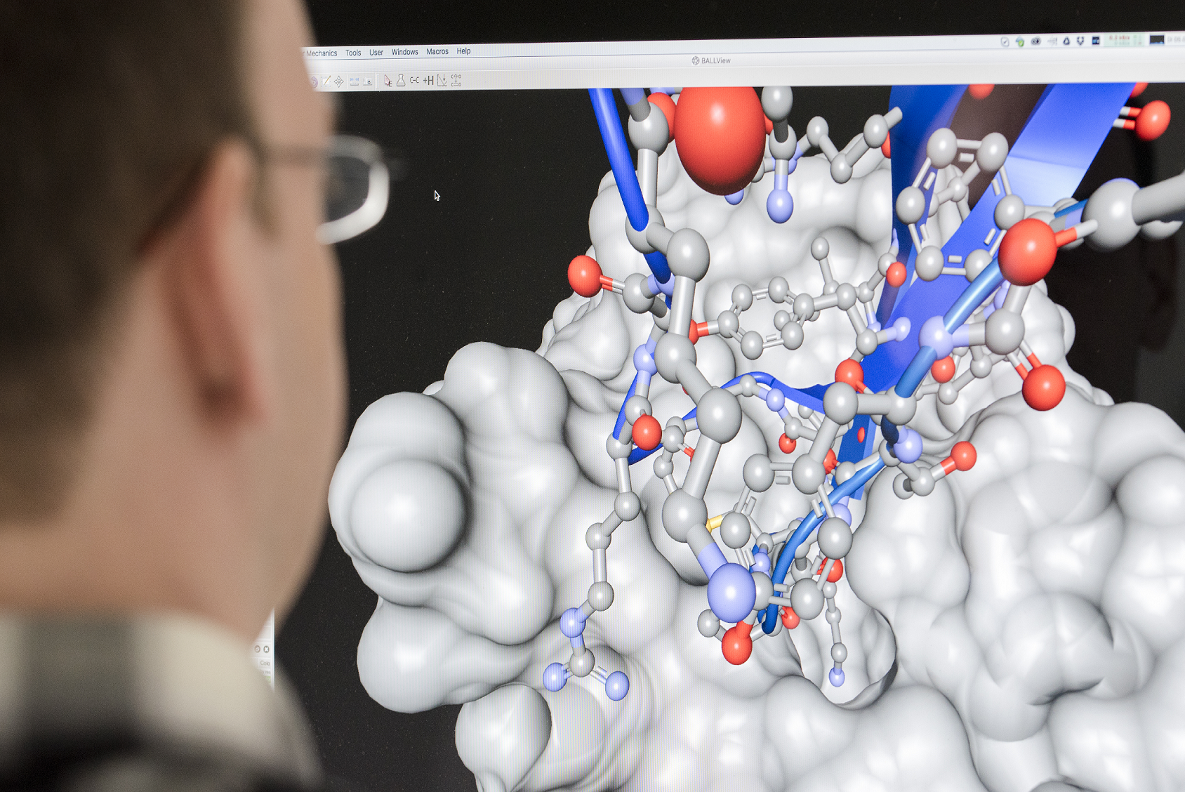 Der Kopf eines Wissenschaftlers vor einem Computerbildschirm mit Molekülmodell.