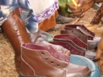 The photo shows good footwear and people sitting in front of the shoes. Only the legs and feet can be seen. They are oedematous. The ground on which the shoes are standing is of a sandy texture and partially covered with straw.